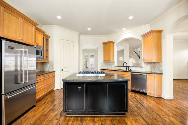 kitchen with a sink, a center island, dark stone counters, built in appliances, and dark wood-style flooring