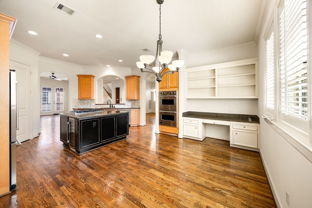 kitchen with visible vents, dark wood finished floors, built in desk, appliances with stainless steel finishes, and arched walkways