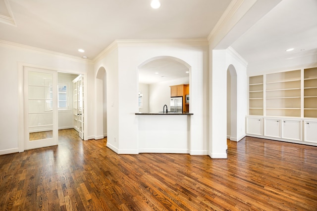 unfurnished living room featuring baseboards, recessed lighting, dark wood-style flooring, a sink, and ornamental molding