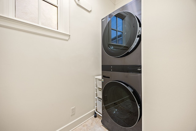 clothes washing area featuring tile patterned flooring, laundry area, stacked washer and dryer, and baseboards