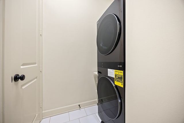 clothes washing area featuring light tile patterned floors, laundry area, baseboards, and stacked washer and dryer