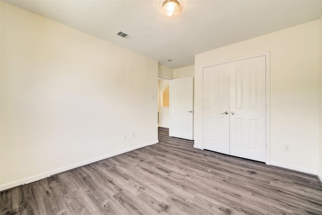 unfurnished bedroom with wood finished floors, visible vents, a closet, and baseboards