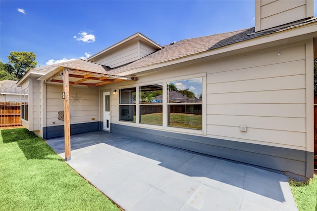 exterior space featuring a lawn, a shingled roof, a patio, and fence