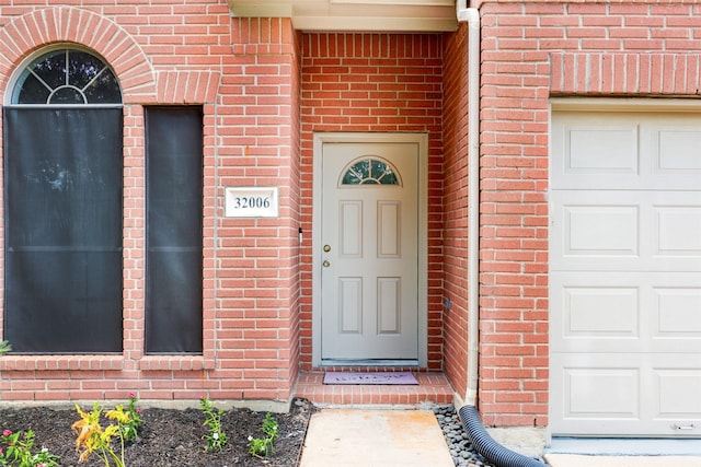 view of exterior entry featuring brick siding and a garage