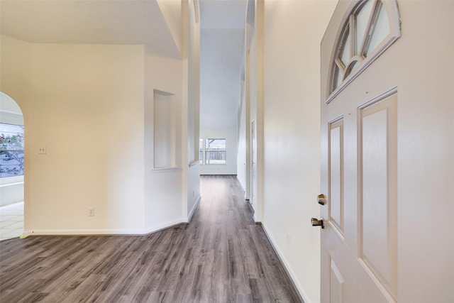 corridor with wood finished floors, arched walkways, a towering ceiling, and baseboards