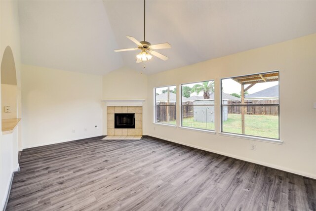 unfurnished living room with a tiled fireplace, wood finished floors, baseboards, and vaulted ceiling