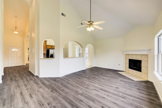 unfurnished living room with visible vents, a tile fireplace, wood finished floors, ceiling fan, and vaulted ceiling