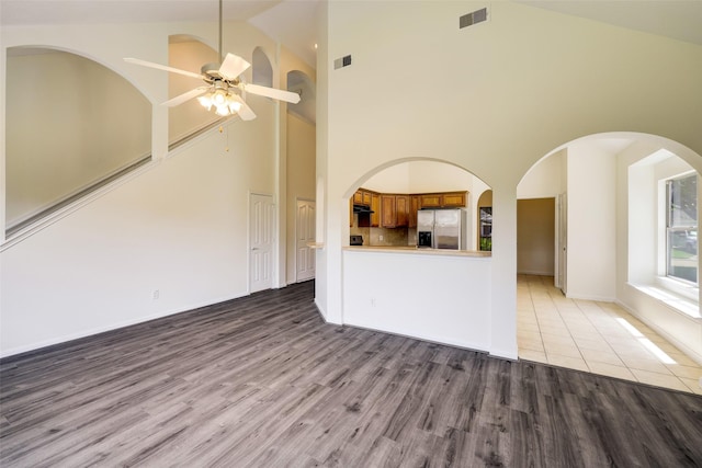 unfurnished living room with ceiling fan, visible vents, high vaulted ceiling, and wood finished floors