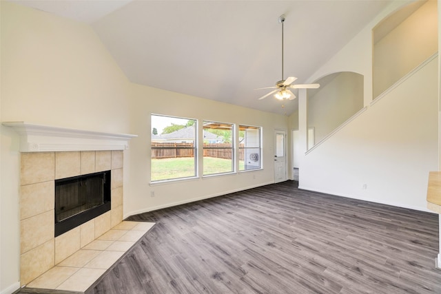 unfurnished living room featuring baseboards, ceiling fan, a tile fireplace, wood finished floors, and high vaulted ceiling