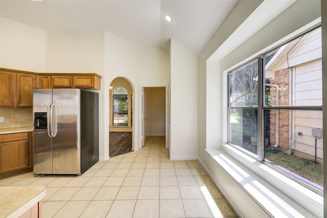 kitchen featuring light tile patterned flooring, arched walkways, brown cabinetry, and stainless steel fridge with ice dispenser