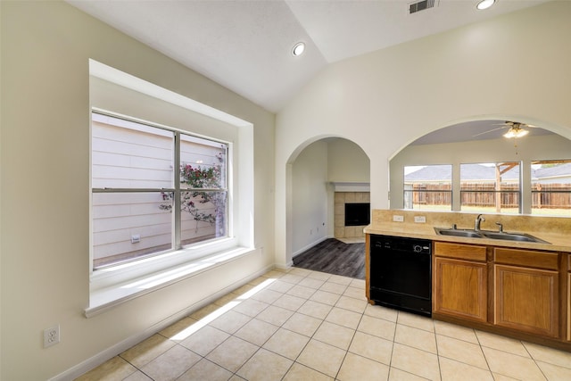 kitchen featuring lofted ceiling, black dishwasher, light tile patterned floors, brown cabinets, and a sink