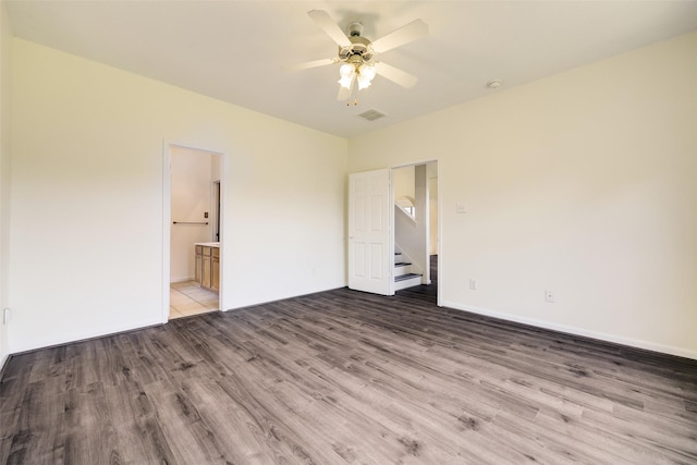 unfurnished bedroom featuring a ceiling fan, wood finished floors, visible vents, baseboards, and ensuite bathroom