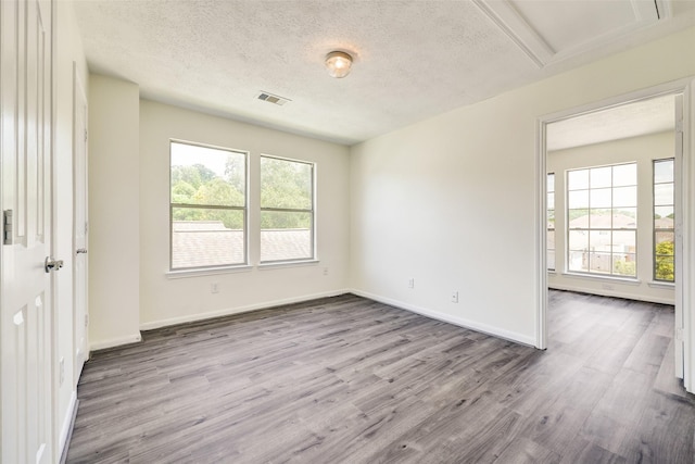 spare room featuring visible vents, wood finished floors, baseboards, and a textured ceiling