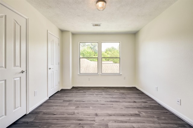 unfurnished bedroom featuring dark wood finished floors, visible vents, a textured ceiling, and baseboards