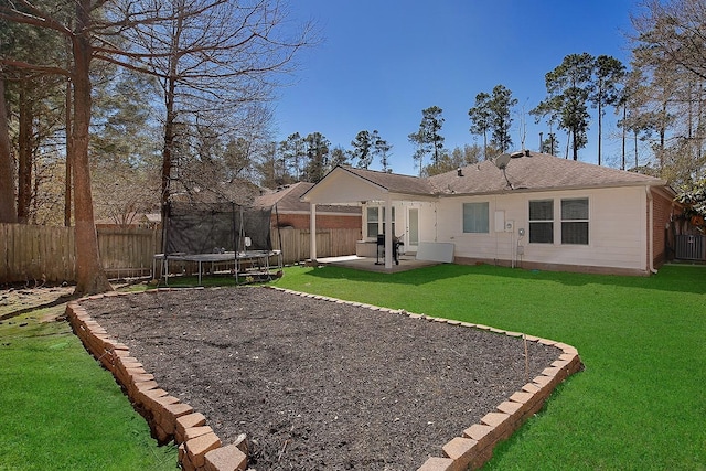 rear view of house with a trampoline, a fenced backyard, a yard, brick siding, and a patio area