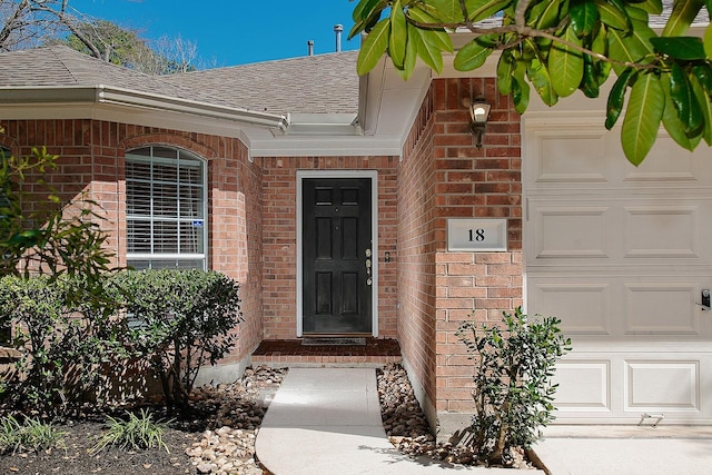 view of exterior entry with brick siding, an attached garage, and a shingled roof