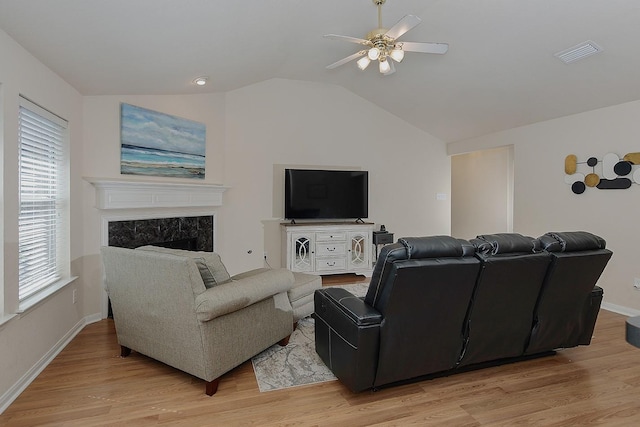 living area featuring vaulted ceiling, visible vents, light wood-style flooring, and a premium fireplace