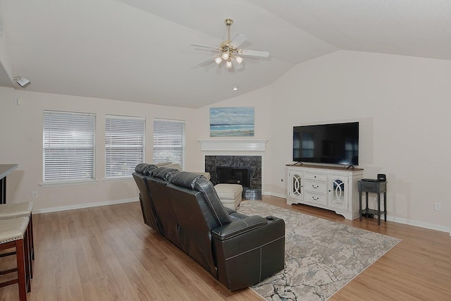 living area with baseboards, ceiling fan, vaulted ceiling, a premium fireplace, and light wood-style flooring