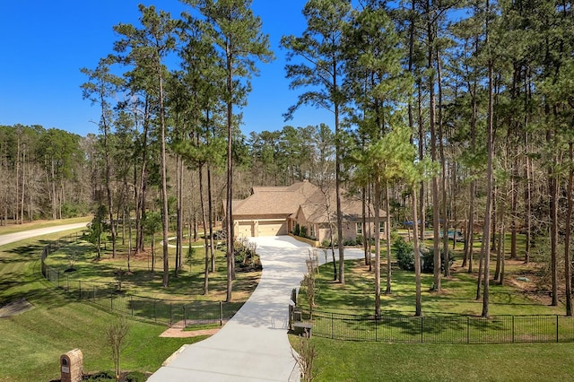 view of front of property with a front lawn, a fenced front yard, concrete driveway, a wooded view, and a garage