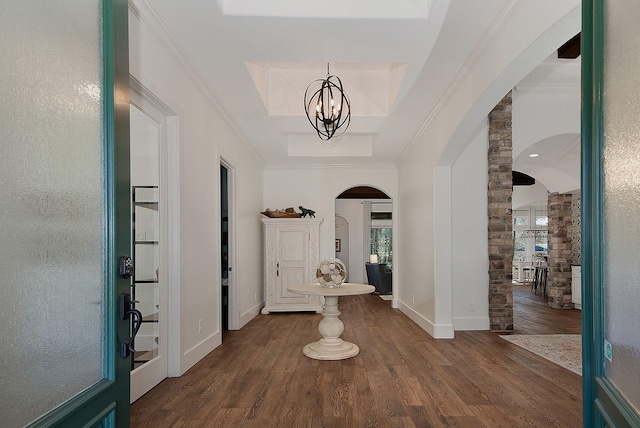 foyer with a tray ceiling, arched walkways, dark wood-type flooring, crown molding, and a notable chandelier