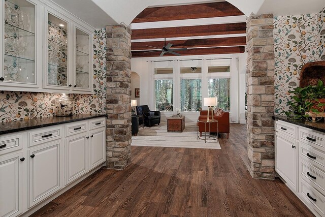 kitchen with dark countertops, glass insert cabinets, beam ceiling, dark wood-style floors, and arched walkways