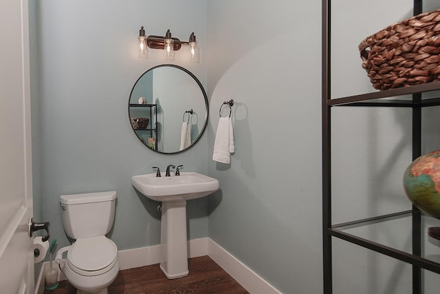 half bath with a sink, toilet, baseboards, and wood finished floors