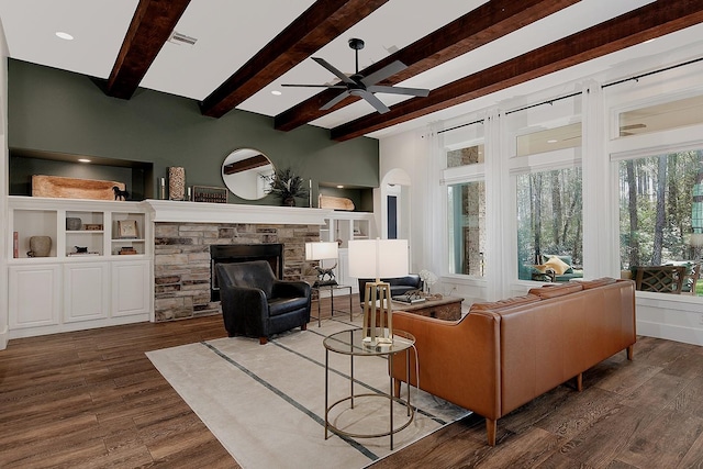 living area with beamed ceiling, visible vents, a ceiling fan, wood finished floors, and a stone fireplace