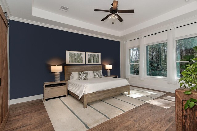 bedroom featuring a tray ceiling, wood finished floors, visible vents, and baseboards