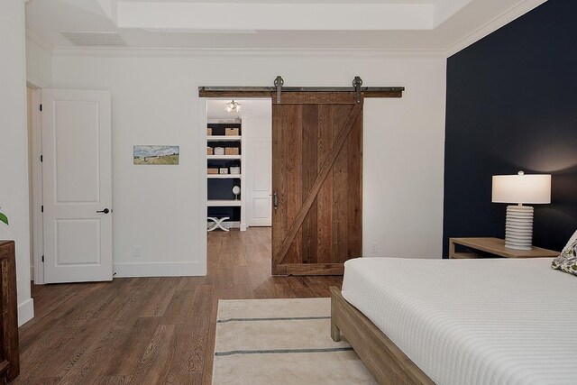 bedroom featuring a barn door, baseboards, wood finished floors, and crown molding