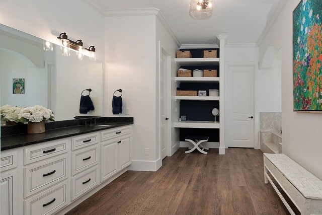 bathroom with crown molding, baseboards, wood finished floors, a bath, and vanity