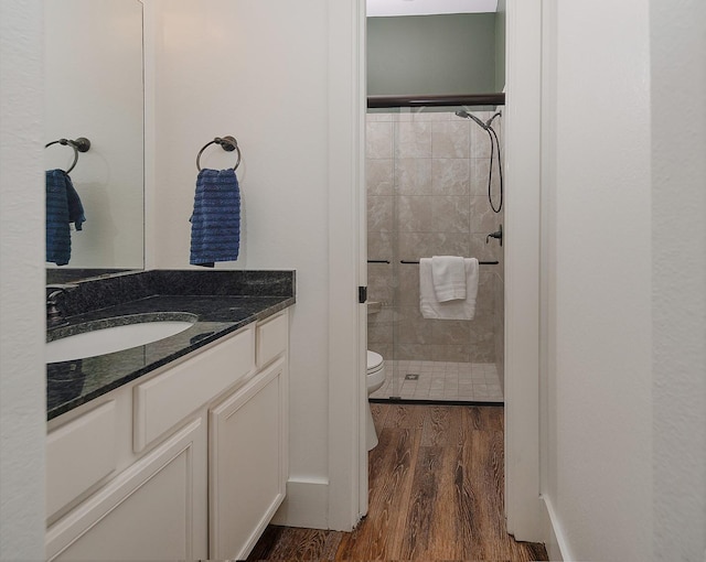 full bathroom featuring baseboards, toilet, a tile shower, wood finished floors, and vanity