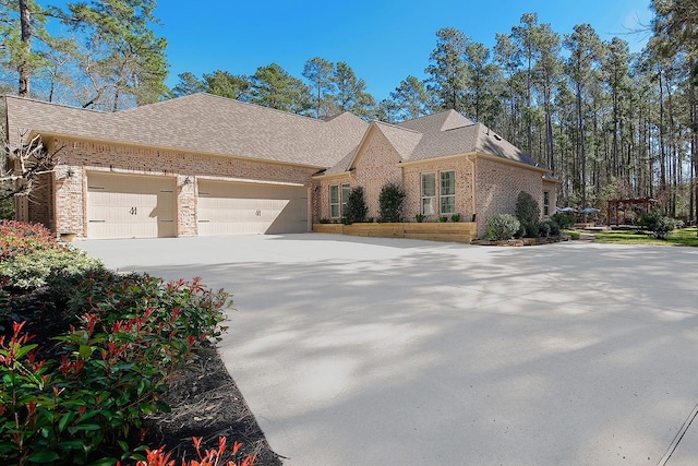 view of front of property featuring a garage, brick siding, driveway, and a shingled roof