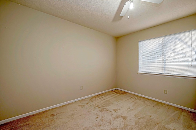 empty room featuring ceiling fan, light colored carpet, baseboards, and a textured ceiling