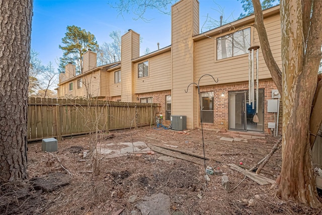 back of house featuring brick siding, central AC unit, a chimney, and fence