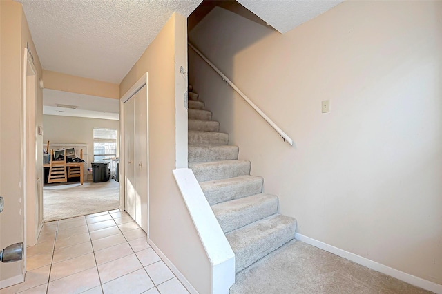 stairway with tile patterned floors, carpet flooring, a textured ceiling, and baseboards