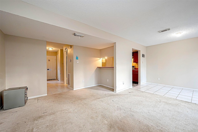 empty room featuring light tile patterned floors, visible vents, light colored carpet, and a textured ceiling