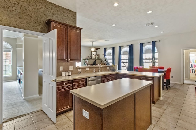 kitchen featuring a kitchen island, dishwasher, light countertops, a peninsula, and light tile patterned flooring