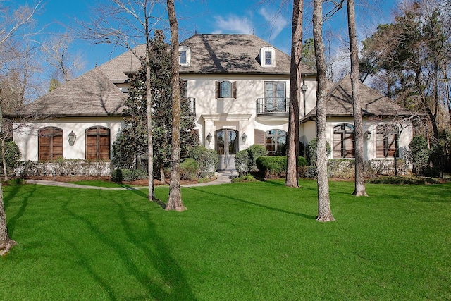 french country home featuring a front yard, a balcony, and stucco siding