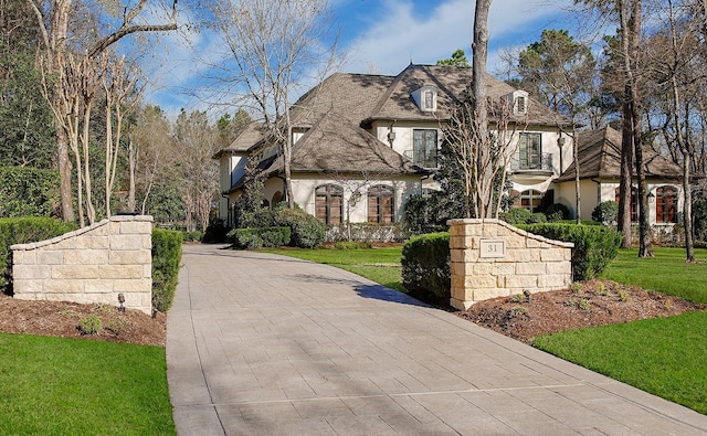 french country home featuring stucco siding, decorative driveway, and a front yard