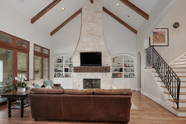 living area featuring built in shelves, baseboards, beamed ceiling, light wood-type flooring, and a fireplace