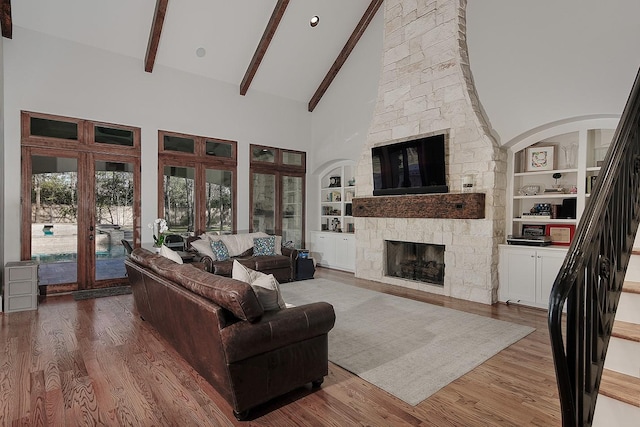 living area with a stone fireplace, beam ceiling, and wood finished floors