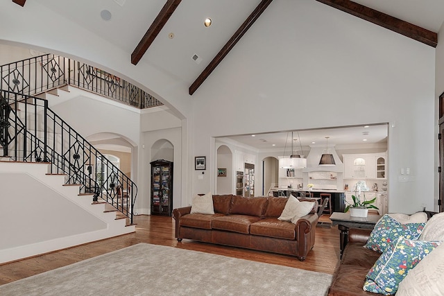 living room with beamed ceiling, stairs, wood finished floors, arched walkways, and high vaulted ceiling