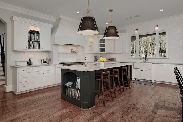 kitchen featuring open shelves, a kitchen island, custom exhaust hood, white cabinetry, and a sink