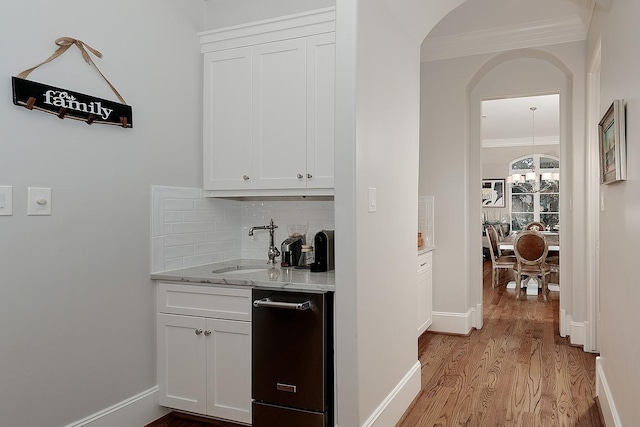 bar featuring light wood-style flooring, a sink, arched walkways, crown molding, and decorative backsplash