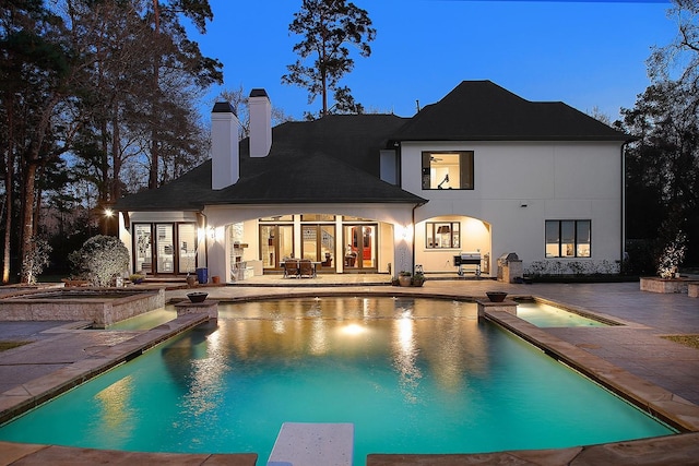 back of house featuring an outdoor pool, stucco siding, a patio, and a chimney