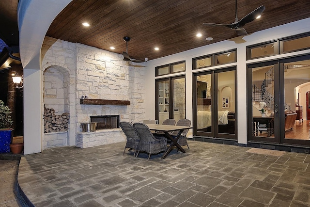 view of patio featuring outdoor dining area, a stone fireplace, ceiling fan, and french doors