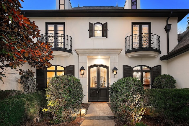 entrance to property featuring stucco siding, french doors, and a balcony