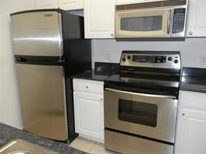 kitchen featuring dark countertops, white cabinets, light tile patterned floors, and stainless steel appliances