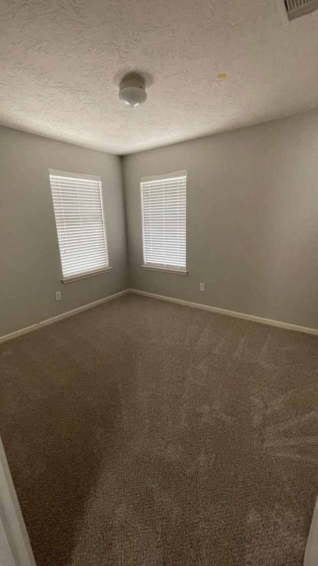 unfurnished room with dark carpet, a textured ceiling, and baseboards