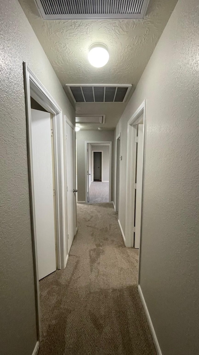 corridor with visible vents, a textured ceiling, a textured wall, and carpet floors